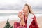 Lady in plaid shirt holding a gift in his hands enjoys beach with Christmas tree. Coastal area. Christmas, New Year