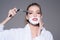 Lady play with sharp blade of straight razor. Girl on dreamy face wears bathrobe, grey background. Woman with face