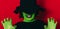 Lady scares in witch costume with green skin color against red background