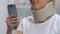 Lady with smartphone in foam cervical collar feeling neck pain, rehabilitation