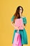 Lady stands on yellow background, holds pink shopping bags.