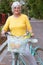 Lady in a yellow blouse crosses the street leading a blue bicycle