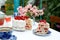 Laid holiday table in the summer garden. Cake, cups, glasses with liquor and a decanter on a table with a white