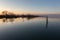 Lake at dusk with perfect reflections, wooden poles in the foreground, trees in the background and soft and warm tones