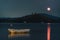 Lake with a fool moon\\\'s pink reflection on it and a wooden boat