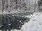 A lake in the forest with snow along the banks.