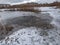 Lake with frozen surface and hole in ice with visible signs of beaver with tree trunks with beaver damage