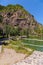 Lake with a gazebo on the shore at the foot of a tall rock on a blue clear sky background