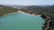 The lake is high in the mountains against the background of forests, hills and the city in the distance, aerial