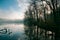 Lake in a late autumn forest, early sun rays shine through bare tree branches on tourist path, reflections on still water surface