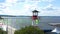 Lake Lighthouse at the city pier. Video. Natural landscape of summer embankment, small lighthouse, waving green flags