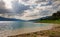 Lake with rocky shore against the backdrop of mountain range covered with forest and blue sky