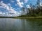 Lake shines green in summer under blowing clouds, white clouds of interesting shape reflect on lake surface