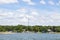 Lakeside homes and boat docks with trees and a transmitter tower in the background under a blue sky with fluffy clouds