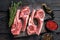 Lamb chops raw meat on bone with salt, pepper and herbs. Black wooden background. Top view