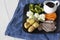 Lamb roast Sunday lunch dinner with vegetables on a aquare black plate, with gravy jug, on a blue tea towel.