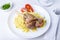 Lamb shin shank with rice, parsley, tomatoes and sauce on a white plate. Traditional dish. Close-up, selective focus