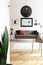 Lamp above couch in white modern apartment interior with plant, posters and armchair. Real photo