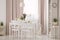 Lamp above table and white chairs in pink dining room interior with plants and drapes. Real photo