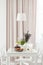 Lamp above white table and chairs in pastel dining room interior with plants and drapes. Real photo