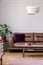 Lamp above wooden table in front of leather couch in minimal flat interior with plant. Real photo