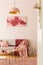 Lamp above wooden tables on pink carpet in loft interior with red poster above grey sofa. Real photo