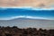 Lanai and shimmering ocean sandwiched by pinkish clouds above and volcanic rock below.