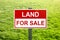 Land for sale sign in green grass field for housing development and construction