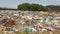 Landfill / dump site with green trees in background. No logos / trademarks visible on dumped garbage