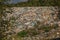 Landfill / dump site surrounded by green trees and mountains in background no logos / trademarks visible on dumped garbage