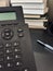 A landline phone is on an office desk on a background of books in a blurred focus.