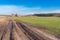 Landscape with agricultural fields and dirty road leading to remote farm-stead