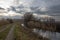 The landscape around the pond. Muddy dirt road and reeds. There are dramatic clouds in the sky