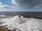 Landscape of Baltic sea and beach with ice and snow formations on the shore in bright sunlight. Frozen ice blocks and sea water in