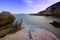 Landscape of blue sea, mountains and textured rocks. Hazy dreamy sky.