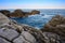 Landscape of blue sea, mountains and textured rocks. Hazy dreamy sky.