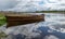 Landscape with calm lake water, wonderful cloud reflections in the lake water, a beautiful brown wooden boat on the lake shore