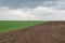 Landscape climate change. The field is half green and plowed, against the backdrop of a cloudy sky