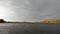 Landscape with cloudy sky over the river and yellow shore in autumn