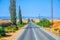 Landscape of Cyprus with cars vehicles riding asphalt road in valley with yellow dry fields, cypress trees and roadside poles