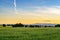 Landscape of fields with wheat green grass with threes and bushes under sunset with mountains in background