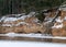 Landscape with frozen river Gauja near Gudu cliffs, view of sandstone cliff from the opposite bank of the river, beautiful red