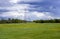 Landscape with green field and forest in the distance with electric power poles extending