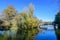 Landscape with grey old bridge and many large green and yellow old trees near the lake in a sunny autumn day in Tineretului Park