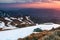 The landscape of the high mountains in snow. The grass and the rocks on the meadow. Sunrise is lightening the horizon. Landscape.