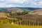 Landscape of hills, country road, cypresses trees and rural houses