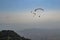 Landscape of hills covered in greenery and fog with people paragliding above at daytime