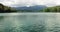 A landscape image of lake with greenish water and green trees and mountains on the background with cloudy sky.