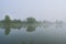 landscape with lake, trees and blue sky with clouds covered in mist