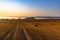 Landscape of a large hilly harvested agricultural wheat field with straw bales at sunrise. Beyond the field is a foggy lowland and